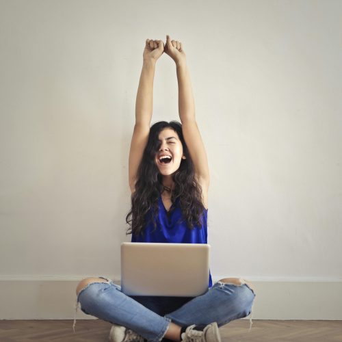 Happy woman with laptop, celebrating success indoors. Arms raised in triumph.